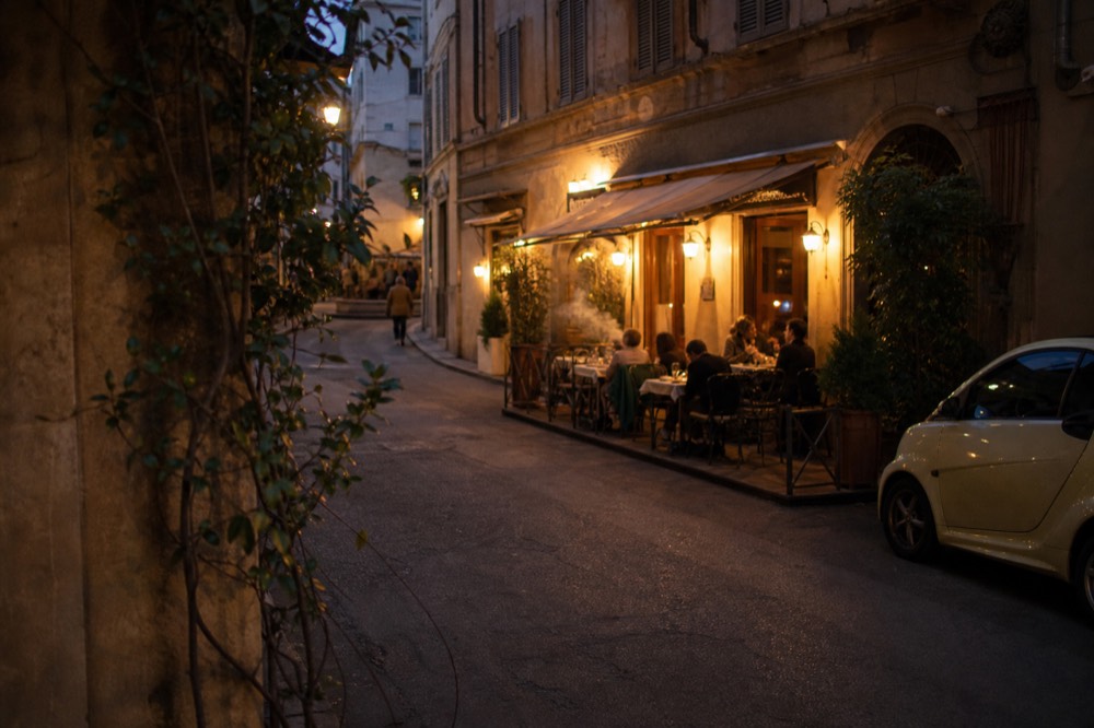 Warm lamplight over an evening street with diners at small tables