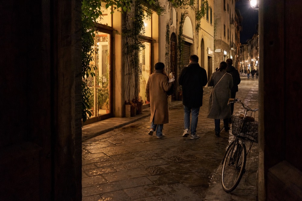 Small group of adults walking together past lit shopfronts in the evening