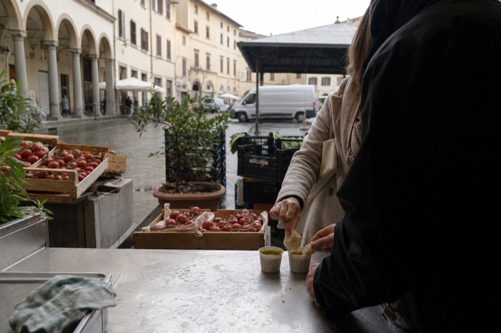 Two people tasting olive oil and bread at a market stall counter
