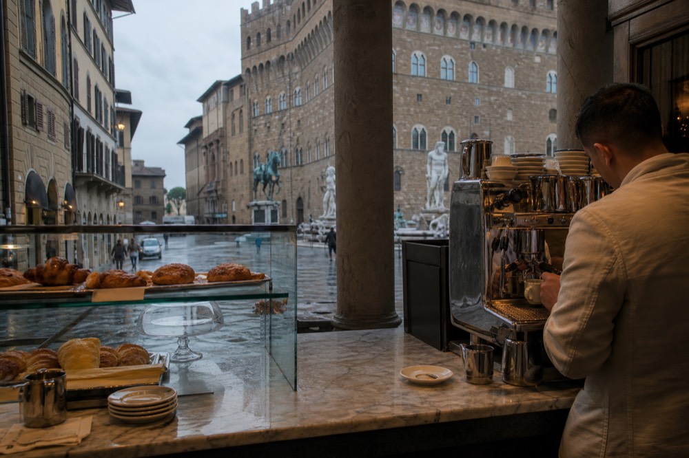Barista pouring espresso behind a marble cafe counter with pastries in a glass case