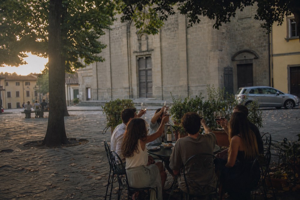 Group of six friends raising wine glasses at an outdoor table in a Florence square