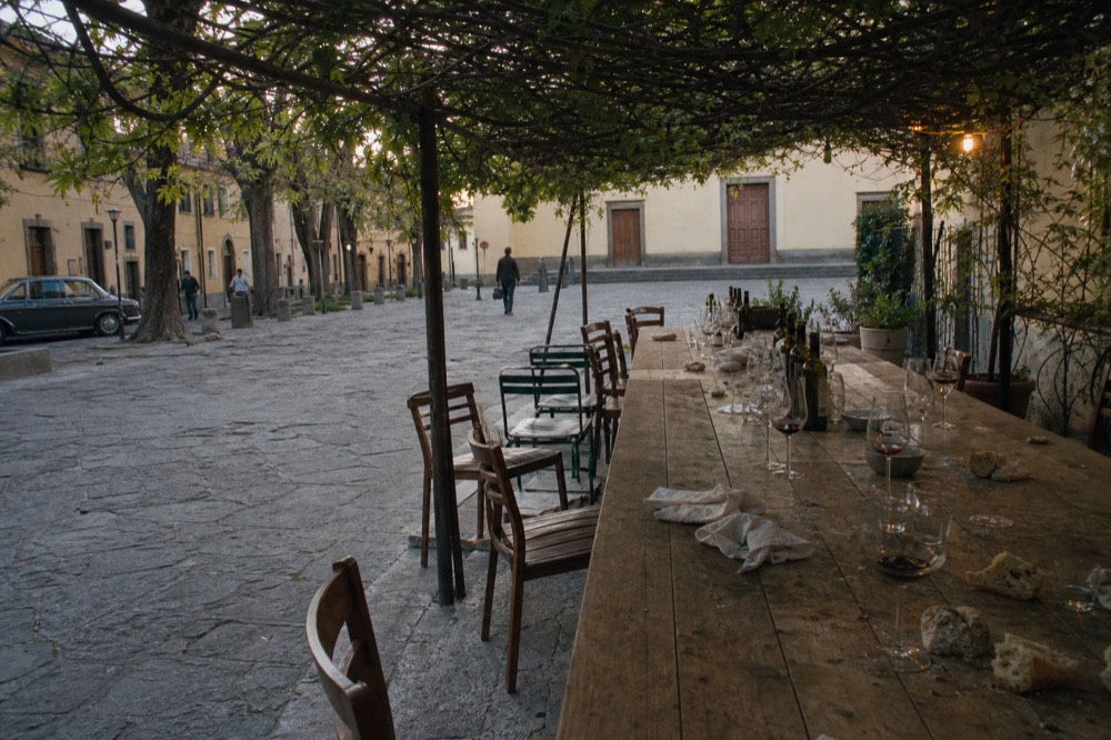 Long table set for lunch outdoors under vines with wine glasses and bread