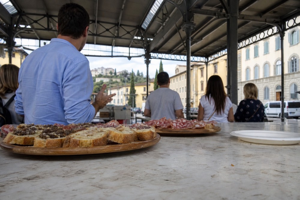 A small group standing at a market counter in Florence while a guide points at trays of food