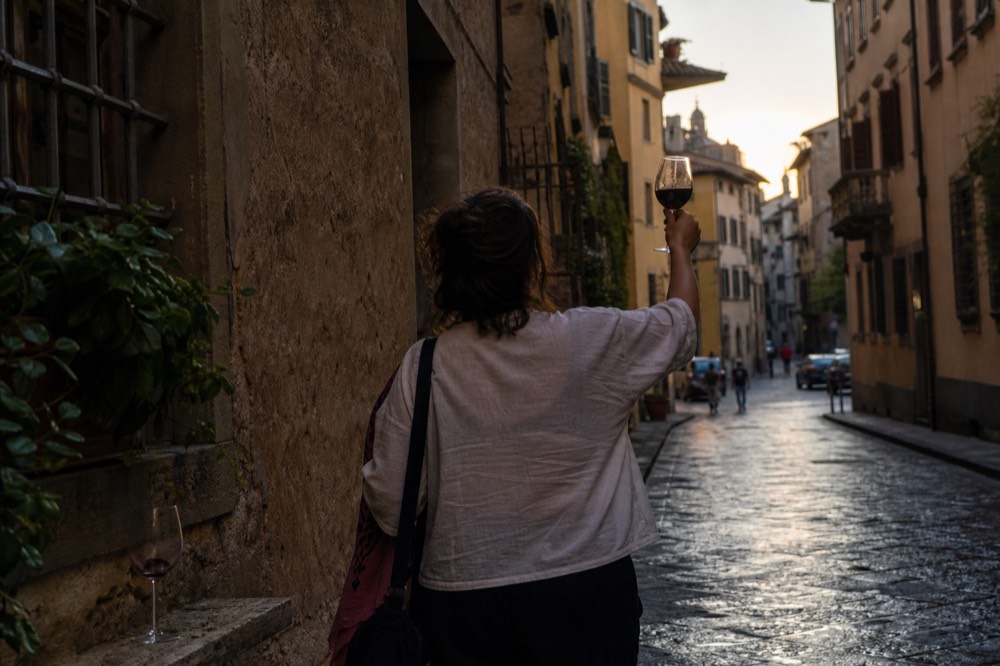 A guide holding a glass of red wine aloft in a narrow Florence street at dusk