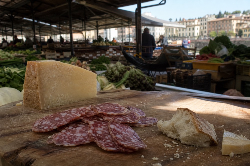 A wooden board with sliced Tuscan salami, pecorino cheese and bread on a market counter