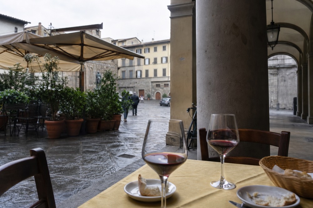 A table set with glasses of red wine, bread and small plates in a Florence trattoria