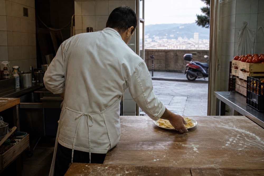 A chef placing a plate of fresh pasta on a wooden table in a market kitchen