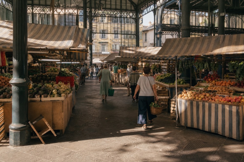 A covered market hall in Florence with produce stalls and shoppers under iron and glass roofing