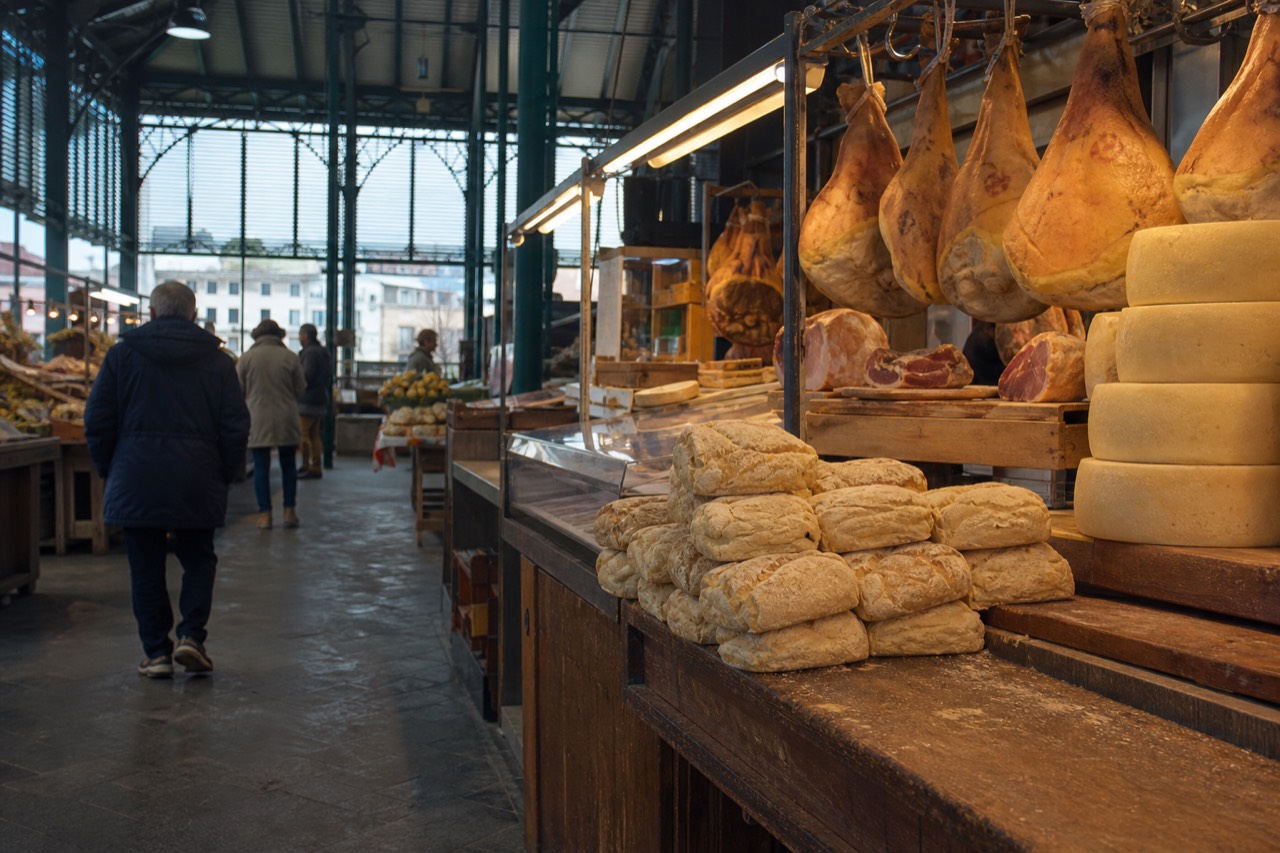 A market stall in Florence with cured meats, cheeses and loaves of unsalted Tuscan bread displayed under warm lights